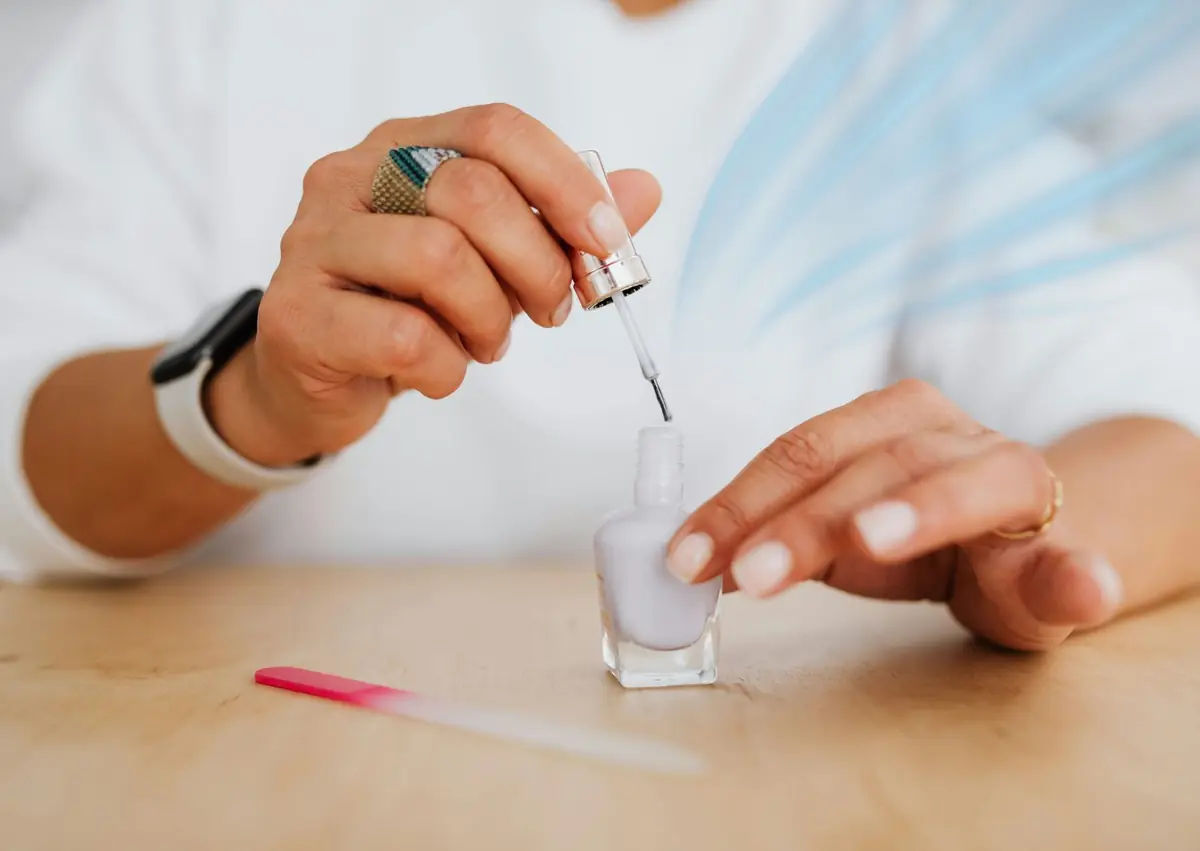 Mano aplicando esmalte semipermanente respirable en uñas cortas naturales durante manicura
