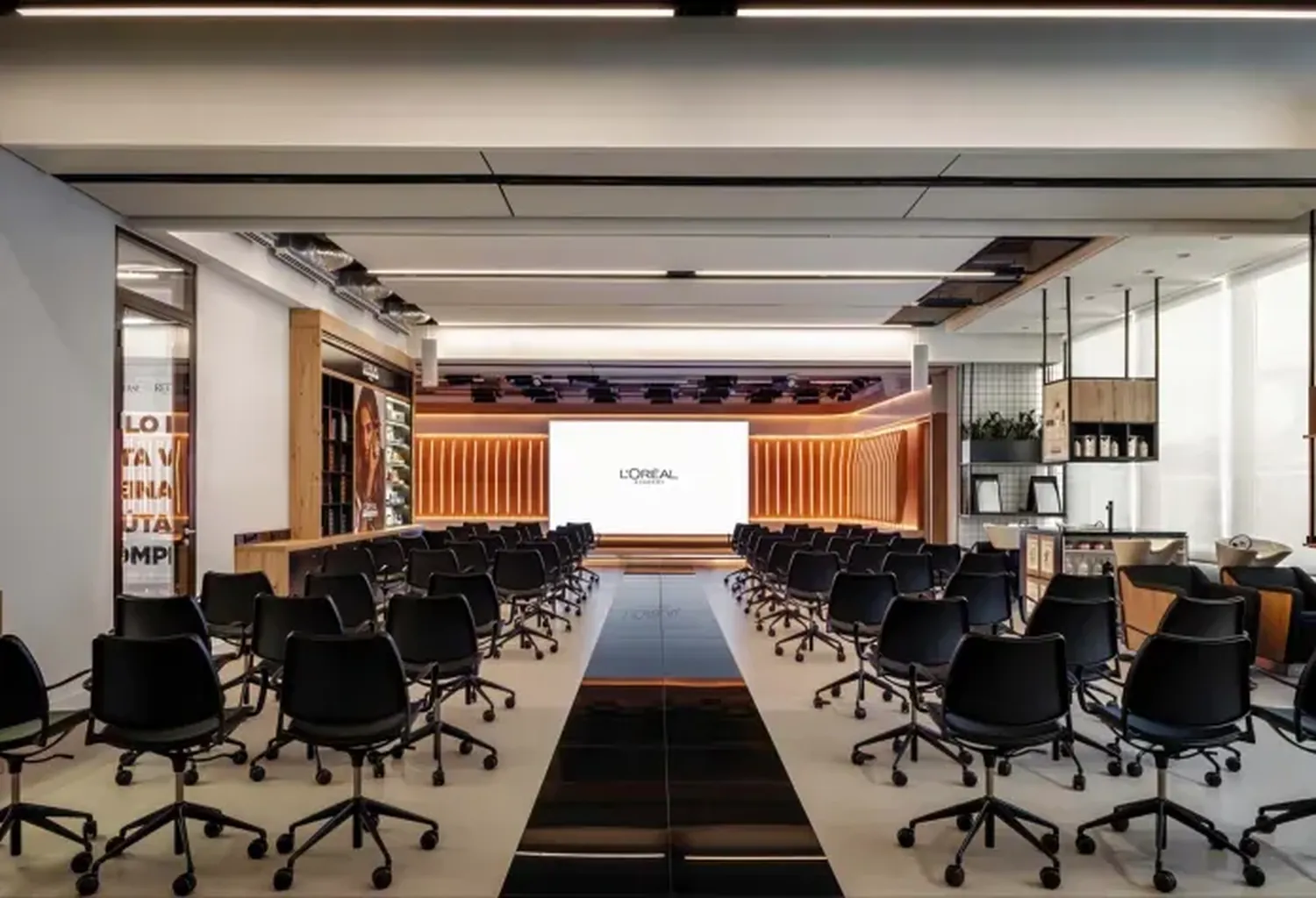 Interior de la sala de formación de L'Oréal Business Academy con sillas negras, pantalla con el logotipo de L'Oréal y acabados en madera