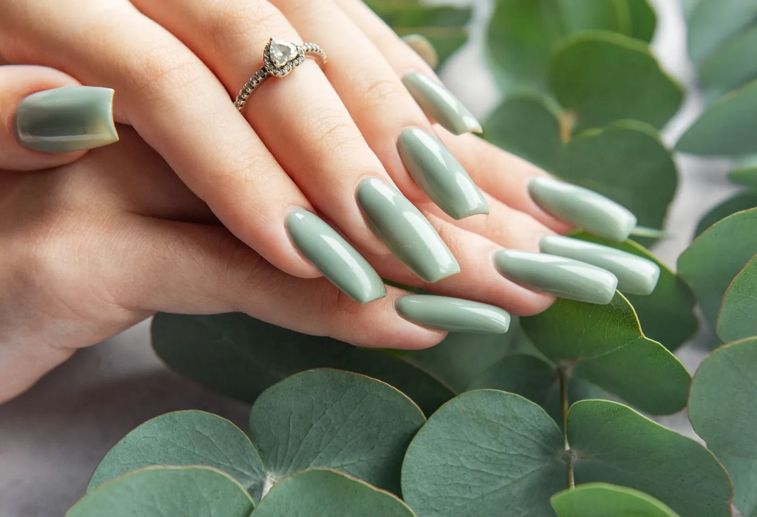 Manos con manicura vegana en tono verde sobre hojas naturales con acabado brillante