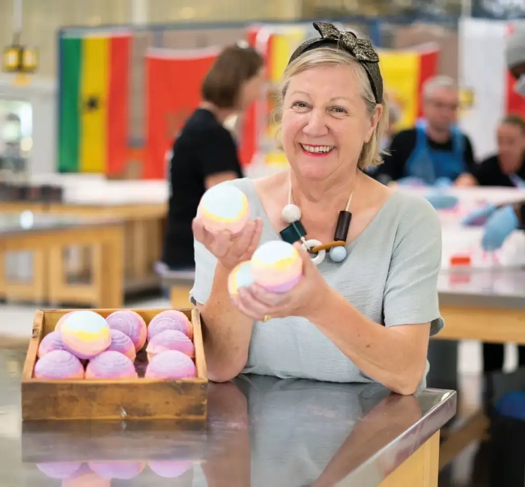 Mujer mostrando bombas de baño artesanales de colores en un taller de cosmética.