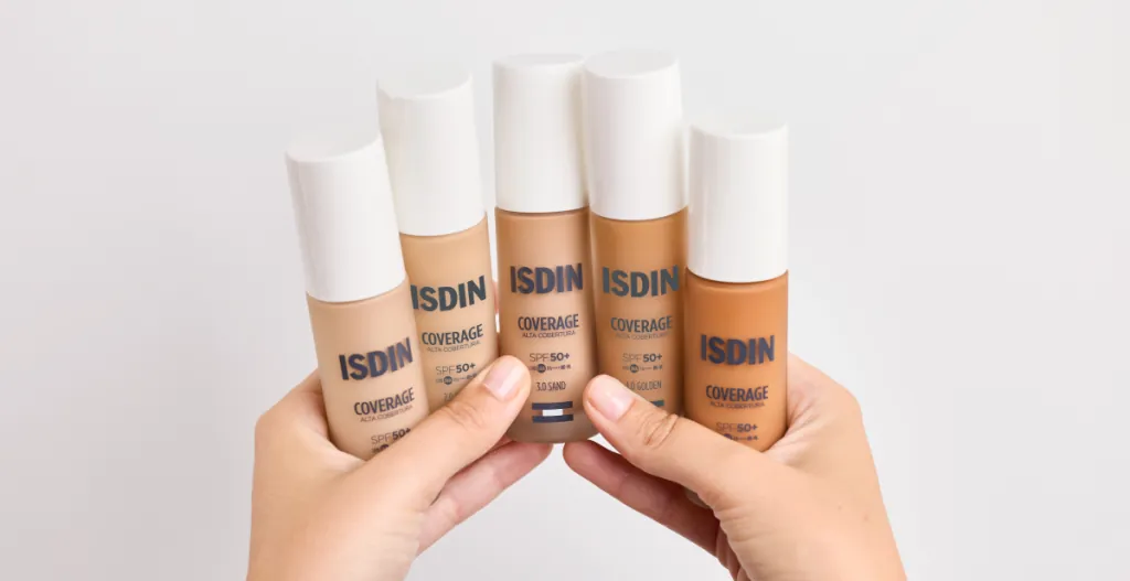 ISDIN Coverage SPF50+ maquillaje corrector con protección solar Gama de maquillajes ISDIN Coverage SPF50+ en diferentes tonalidades sostenidos por una persona para cubrir imperfecciones y proteger la piel del sol.