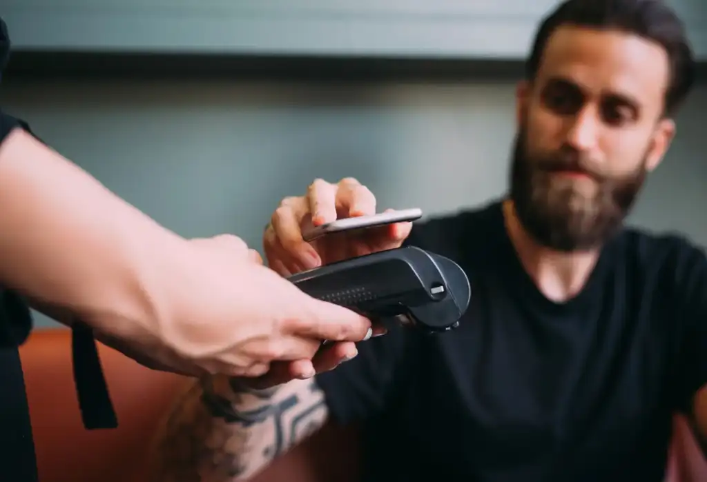 Cliente realizando un pago contactless con tarjeta o móvil en una barbería moderna tras recibir un servicio de cuidado masculino.