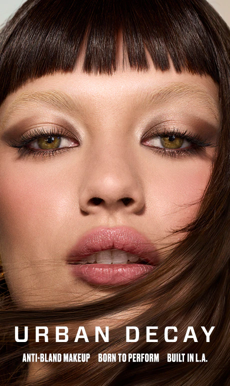 Primer plano de una modelo con maquillaje en tonos neutros y pestañas definidas en una campaña publicitaria de Urban Decay.