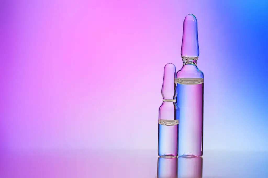 Ampollas de vidrio con solución cosmética sobre fondo degradado en tonos rosa y azul, representando activos concentrados y biotecnología aplicada al cuidado de la piel.
