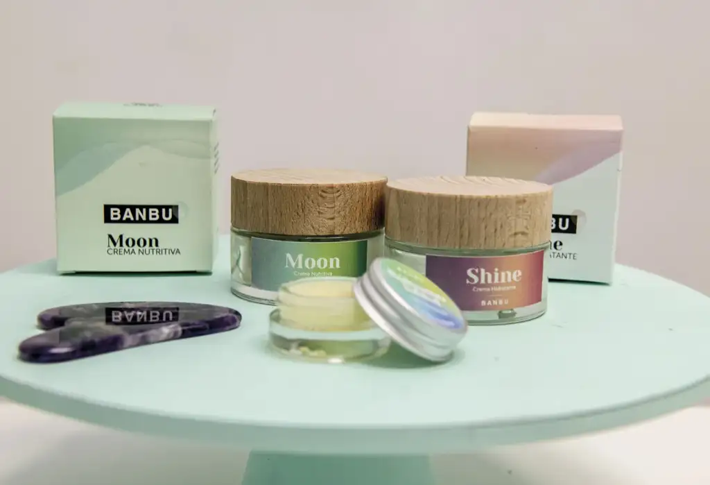 Productos de cosmética natural Banbu con cremas faciales en envases de vidrio y tapas de madera sobre una superficie de color pastel.