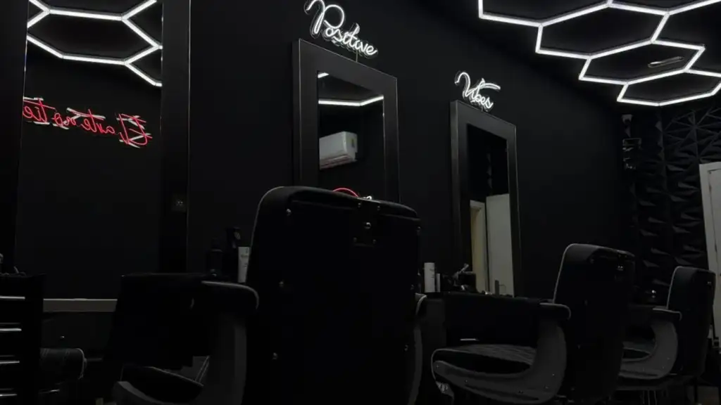 Interior de una barbería premium con sillones profesionales, iluminación LED geométrica y decoración moderna en tonos oscuros.
