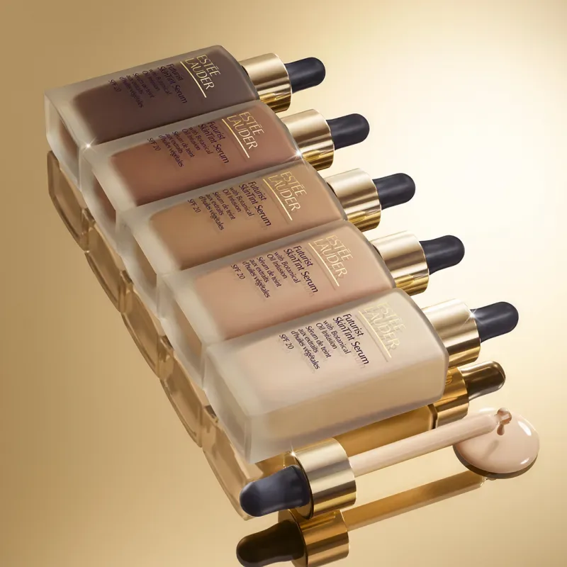 Estée Lauder Futurist SkinTint Serum SPF 20 Gama de tonos de Estée Lauder Futurist SkinTint Serum SPF 20 presentada sobre fondo dorado con aplicador y textura del producto.