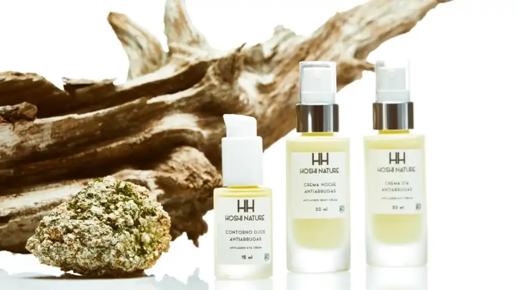 Productos cosméticos antiedad de Hoshi Nature junto a elementos naturales sobre fondo claro, incluyendo contorno de ojos y cremas faciales.