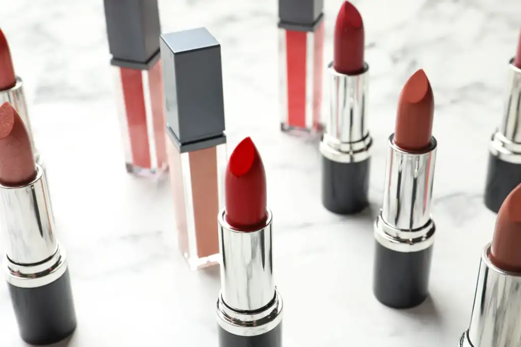 Labiales y brillos de labios: tendencias de maquillaje y cosmética de color Colección de barras de labios y glosses en distintos tonos rojos, nude y rosados dispuestos sobre una superficie de mármol.