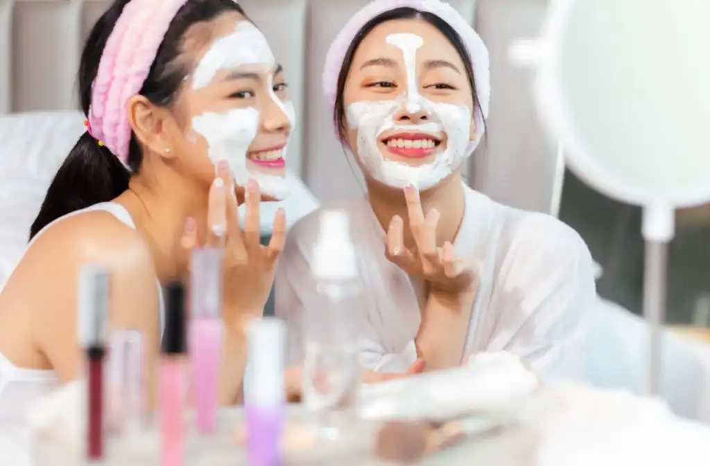 Dos mujeres aplicándose una mascarilla facial hidratante durante una rutina de cuidado de la piel frente al espejo.