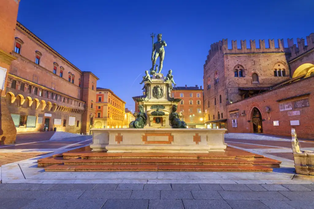 Vista de la Piazza del Nettuno en el centro histórico de Bolonia, Italia, al atardecer, con la Fuente de Neptuno y edificios históricos.
