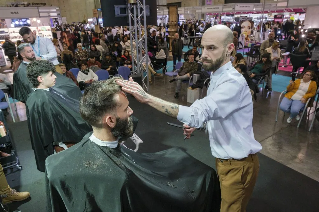 Demostración de barbería profesional en evento del sector Barbero realizando una demostración de corte masculino sobre el escenario de una feria profesional de peluquería y barbería ante el público asistente.