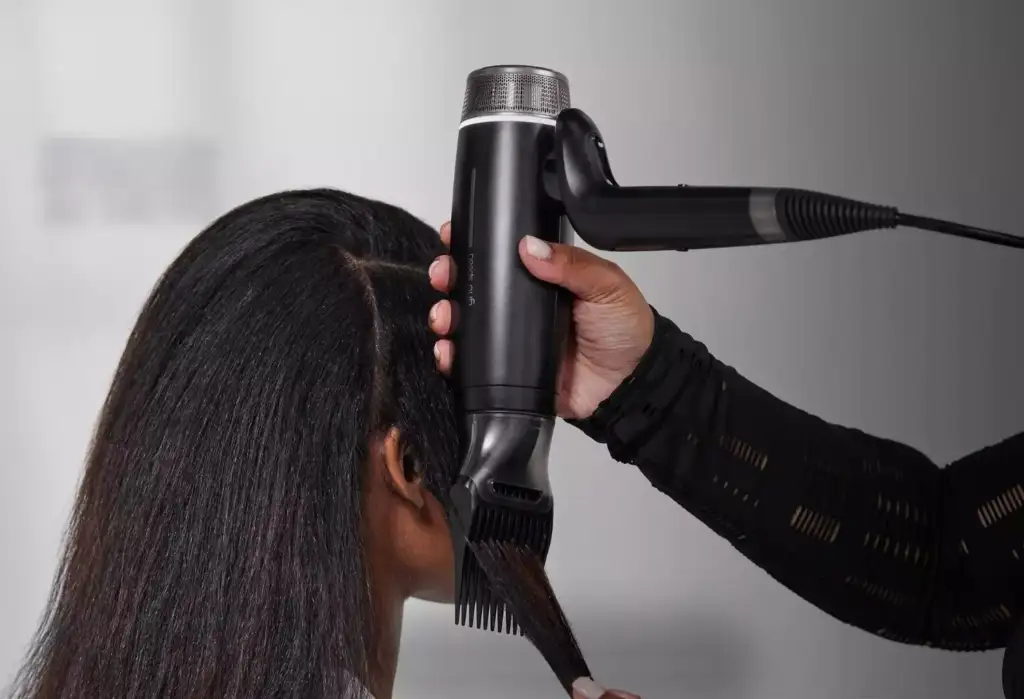 Secador profesional GHD Speed utilizando el peine concentrador sobre cabello texturizado para facilitar el secado y el alisado.