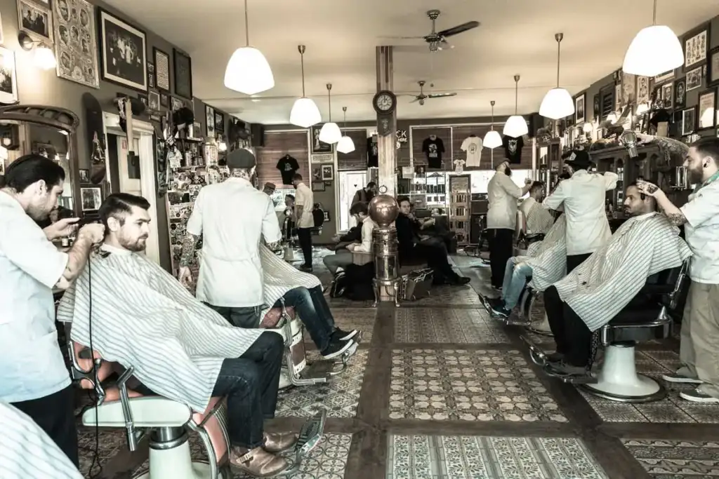 Interior de la barbería Schorem en Rotterdam, cuna de la marca Reuzel, con varios barberos atendiendo a sus clientes.