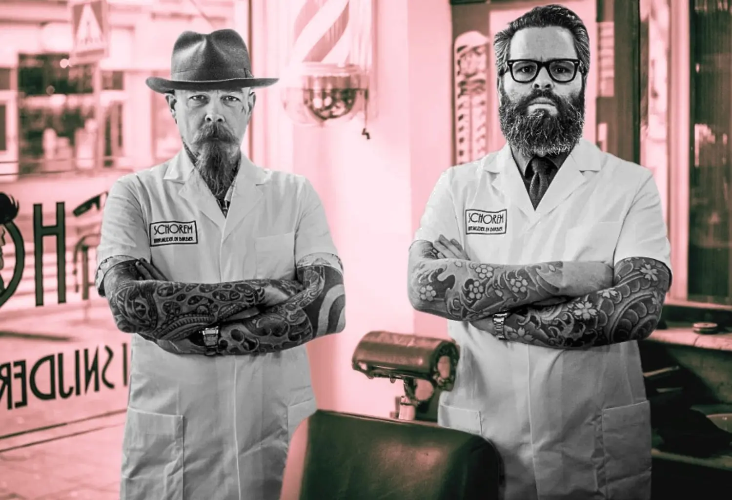 Dos barberos de Schorem Barbers posan con los brazos cruzados en el interior de una barbería clásica, representando el estilo tradicional que ha influido en la barbería moderna.