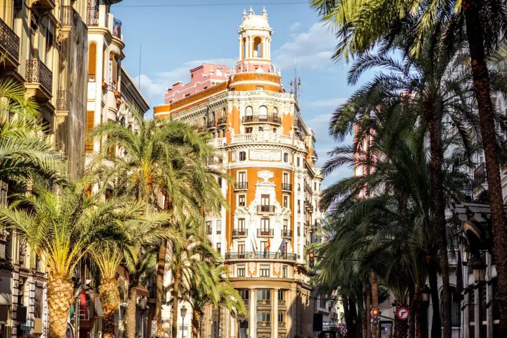 Valencia modernista entre palmeras y arquitectura histórica Vista urbana de Valencia con edificios modernistas emblemáticos, palmeras y arquitectura histórica iluminada por el sol.