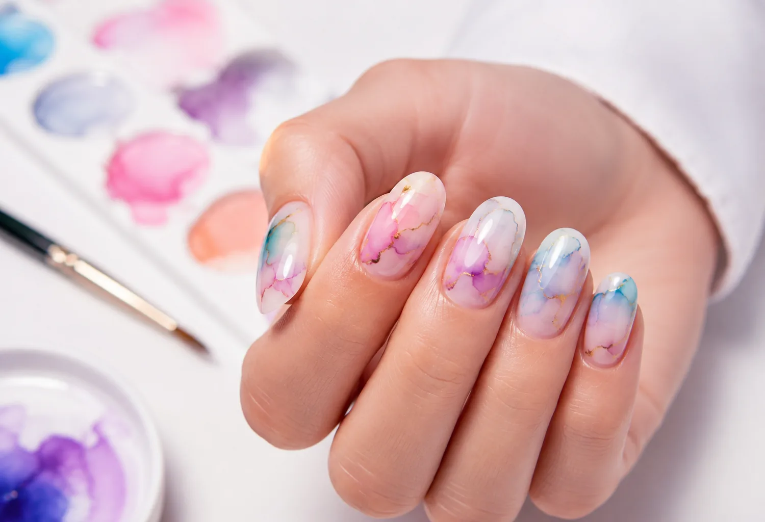Primer plano de una manicura Watercolor con efecto acuarela en tonos pastel y acabado brillante sobre uñas almendradas.