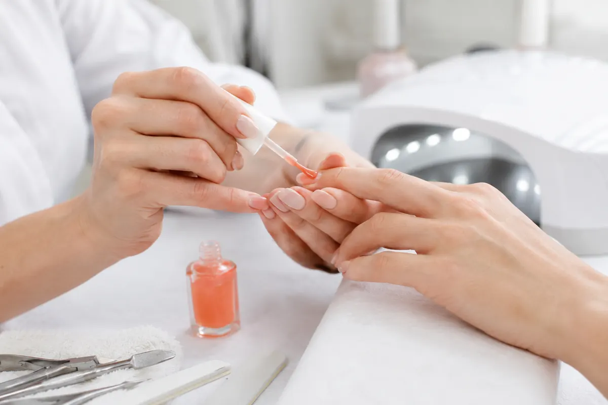 Profesional aplica esmalte gel translúcido coral antes del curado UV LED