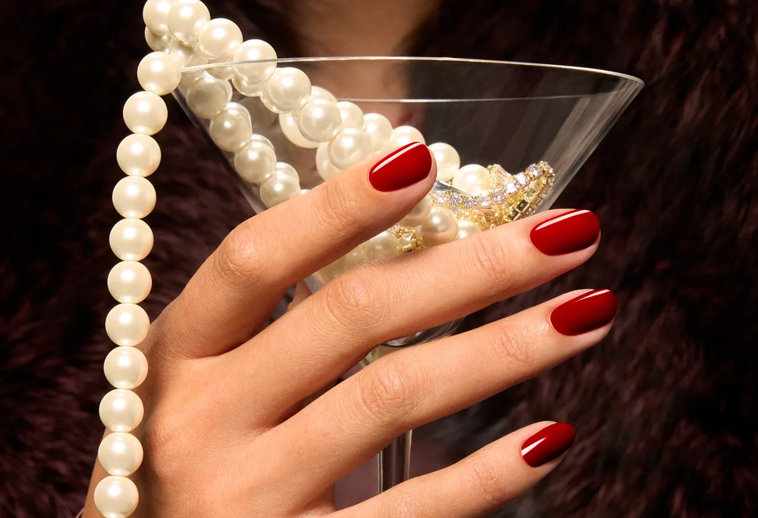 Mano con manicura roja, copa y collar de perlas en la campaña OPI Most Requested