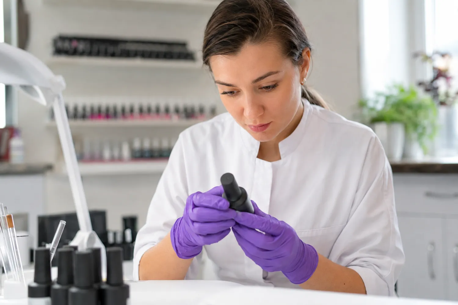 Profesional de manicura con guantes revisa un frasco de producto en el salón