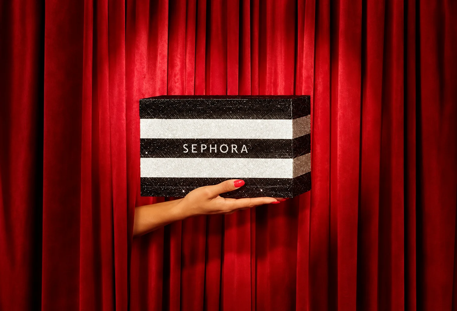 Mano con manicura roja sosteniendo una bolsa Sephora ante cortinas rojas
