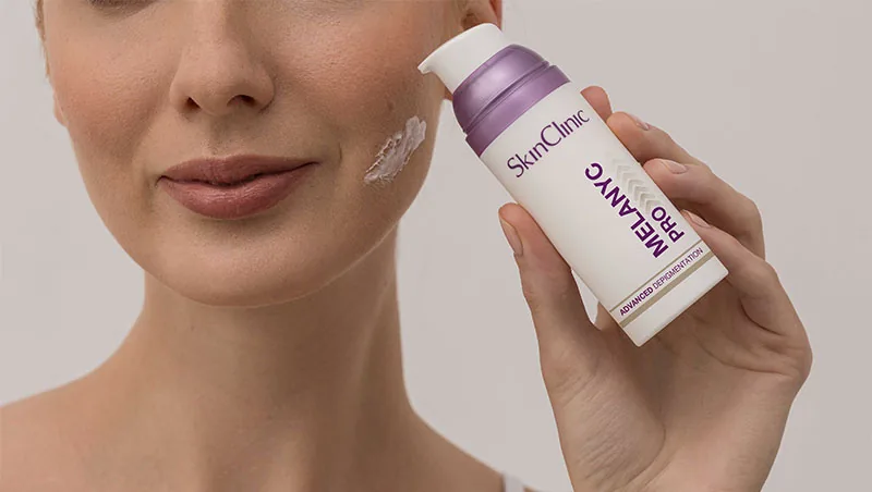 Mujer con crema en la mejilla mostrando el envase de Melanyc Pro de SkinClinic