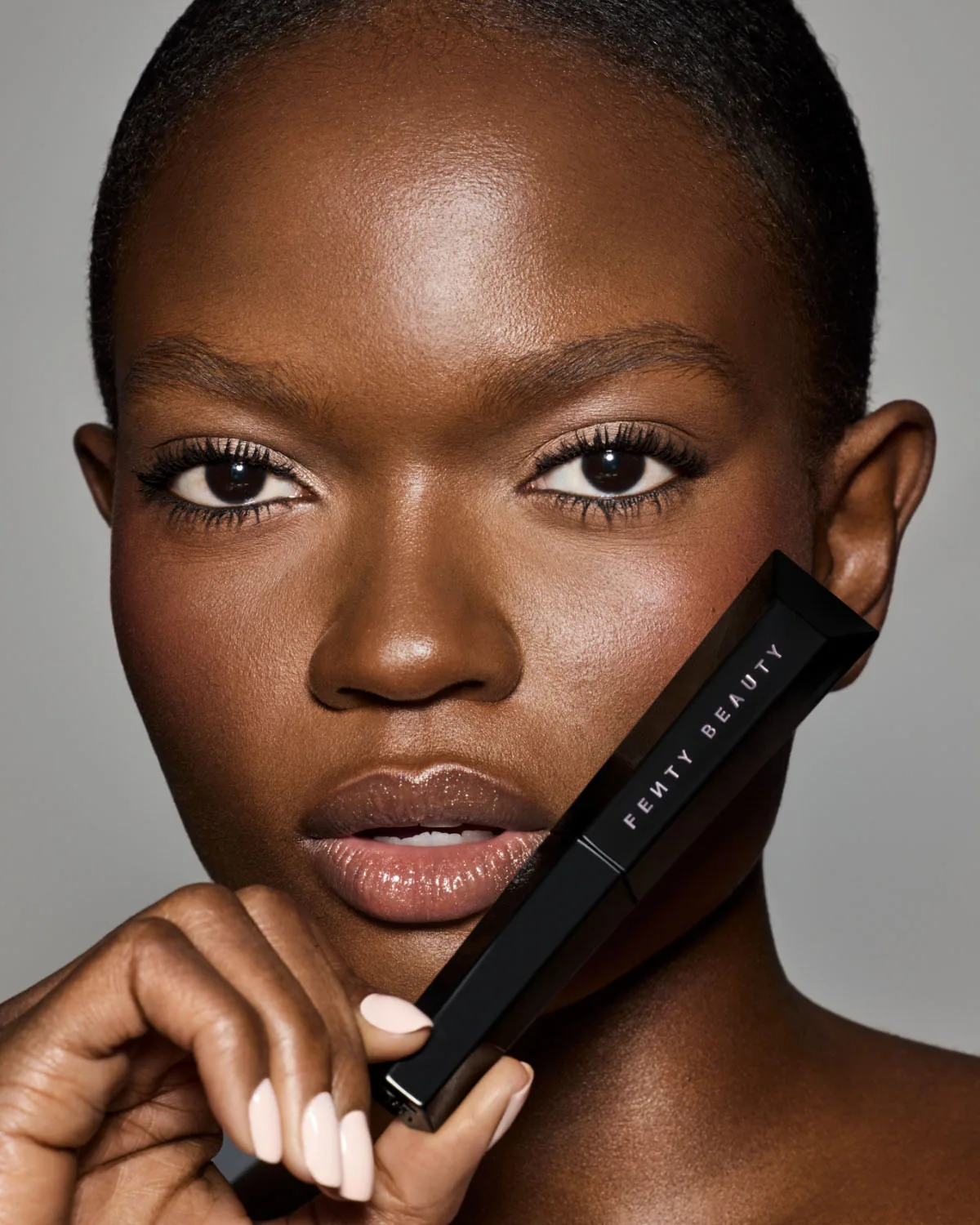 Modelo sosteniendo un envase negro de Fenty Beauty junto al rostro