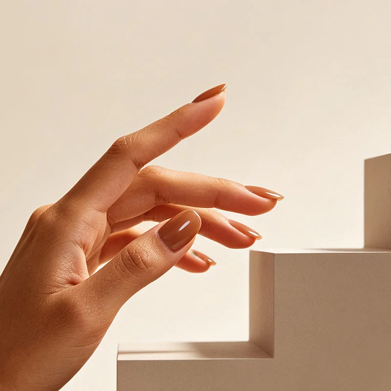 Mano con uñas ovaladas marrones sobre fondo beige