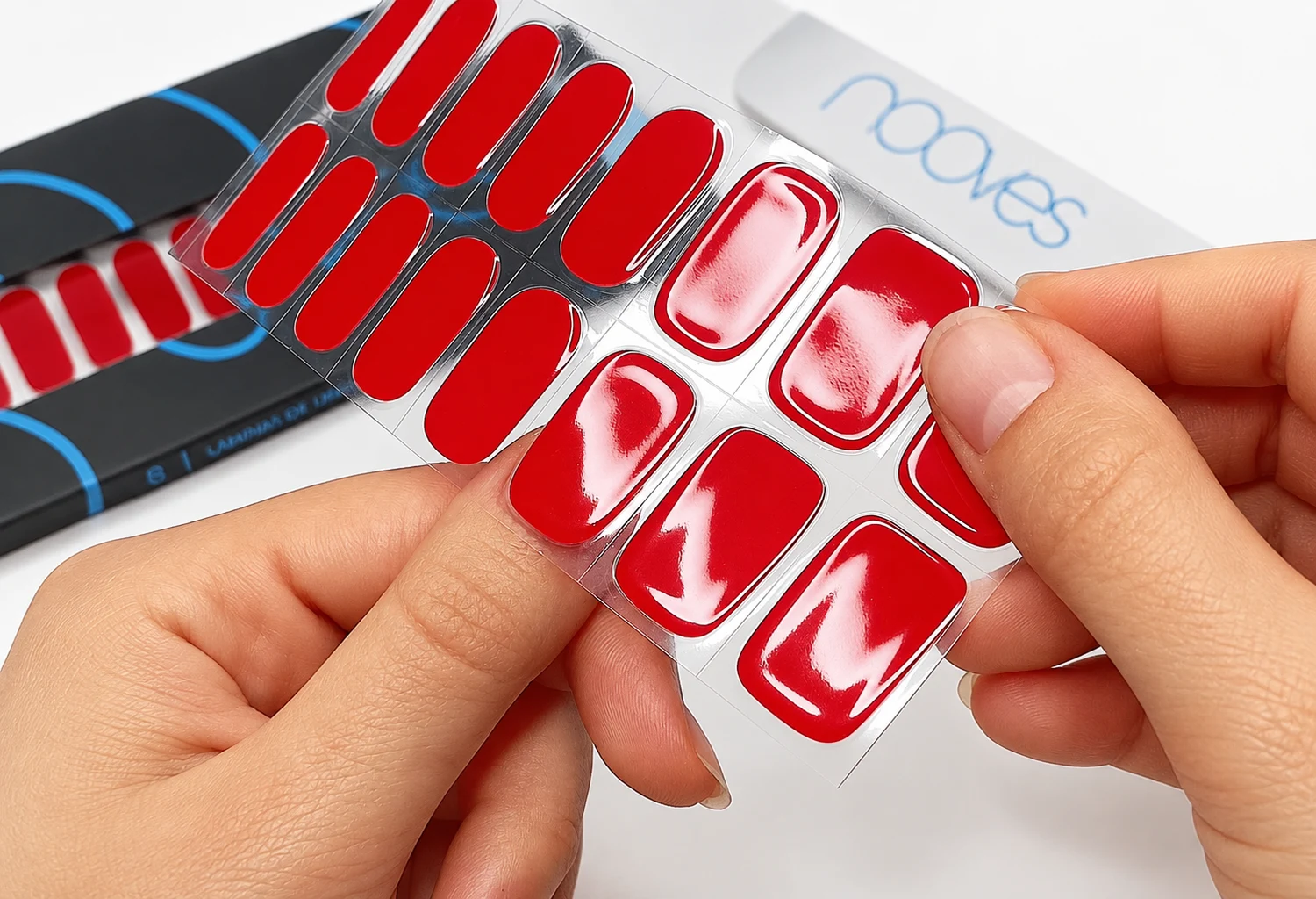 Láminas rojas NOOVES y manicura junto al envase de la marca